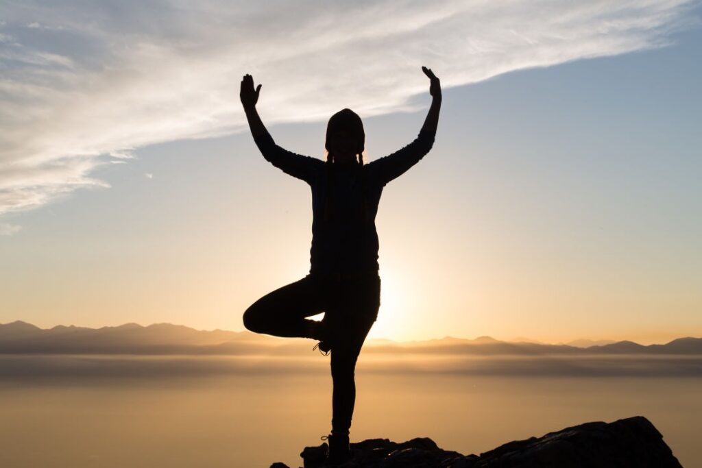 Woman practicing yoga in tree pose on a mountain at sunrise