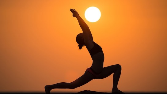 Silhouette of woman doing warrior yoga pose during sunset with sun in background