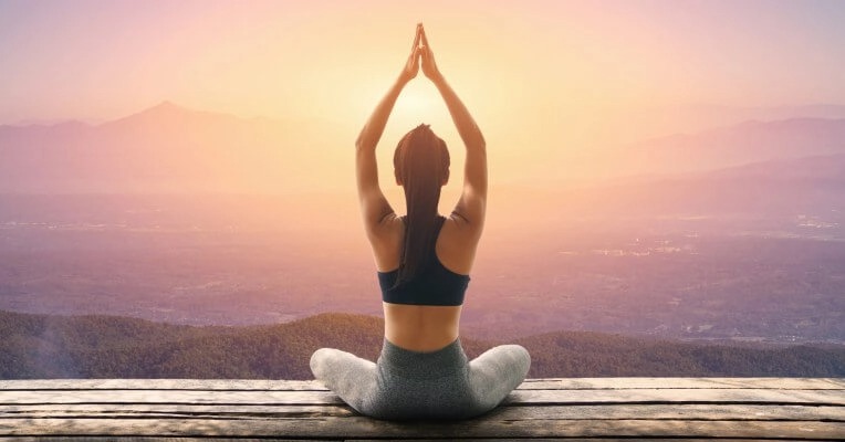 Woman practicing Kundalini Yoga in a seated posture at sunrise overlooking mountains