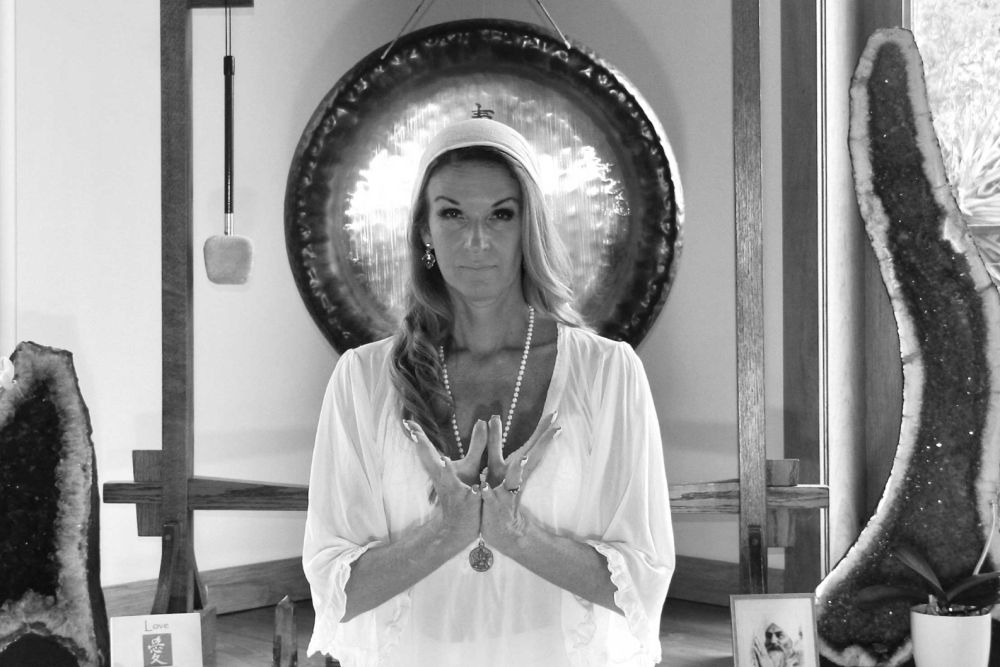 Kundalini yoga teacher standing in front of gong with crystals in a meditation room